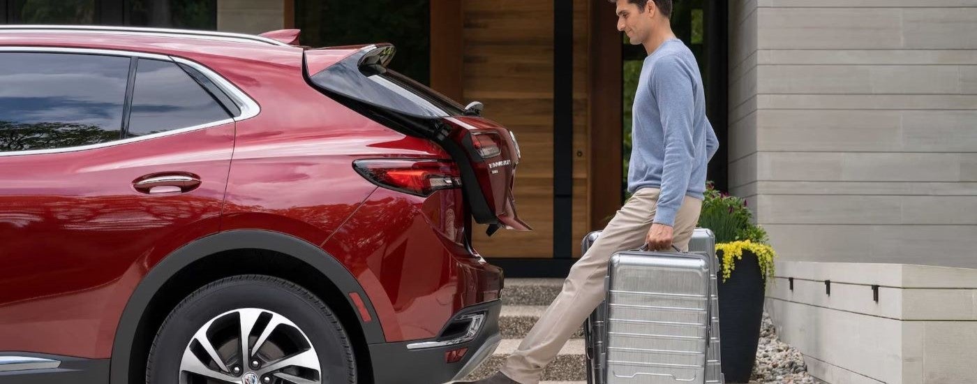 A person is shown stowing luggage in a red 2023 Buick Envision.